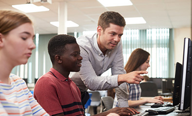 A man instructing a person sitting at a computer